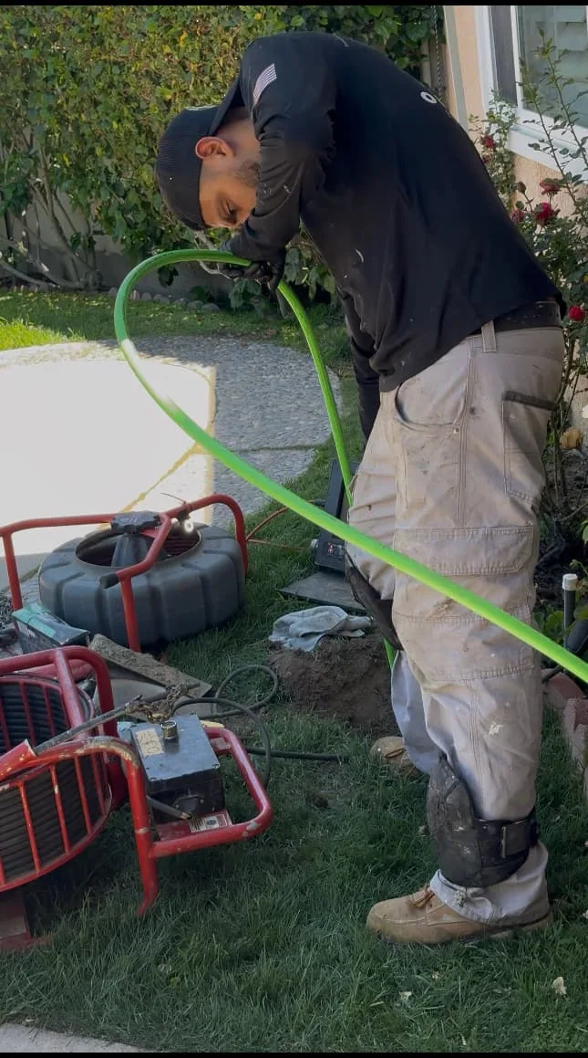 Technician handling a high-pressure drain-cleaning hose and equipment at a residential jobsite