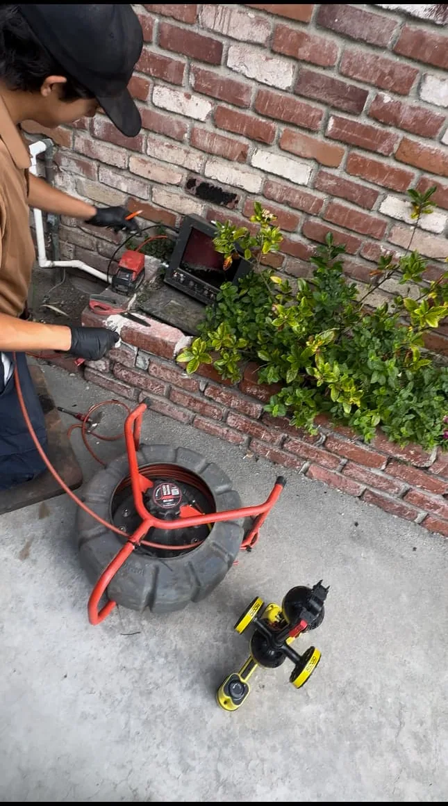 Technician operating sewer camera inspection equipment beside a residential brick wall