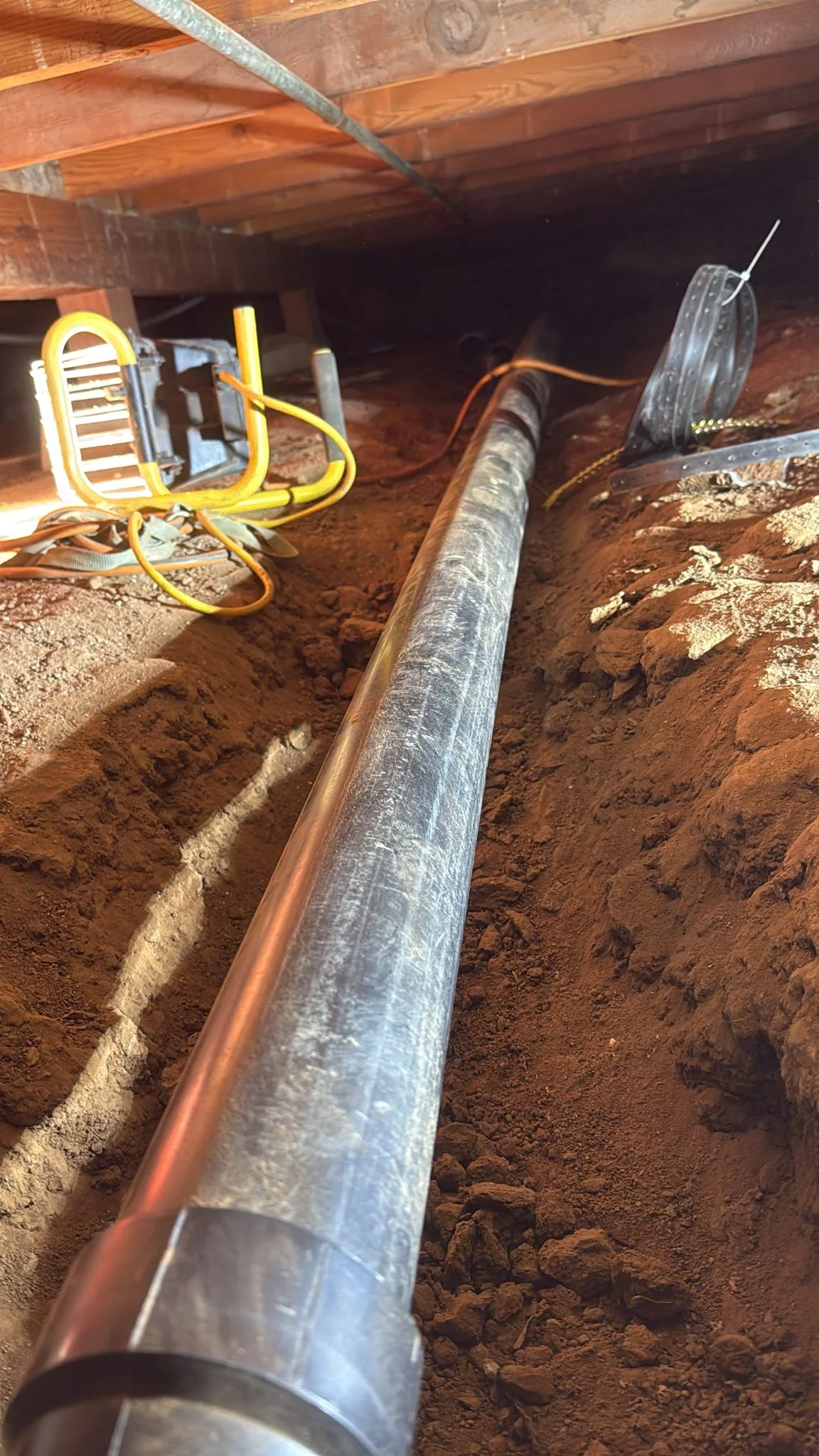 Underground sewer pipe replacement project in an excavated trench below a home